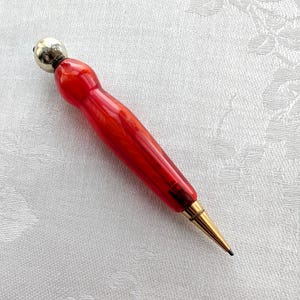 May include: A mechanical pencil featuring a vibrant, translucent red marbled barrel with a rounded, polished silver-tone metal cap at the top and a slender, gold-tone metal tip at the writing end, showcasing a sleek and functional design.