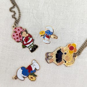 Hooray for the 1980s! Four-piece set including Strawberry Shortcake Necklace, Smurf Ring and Pendant and Cabbage Patch Kid Necklace