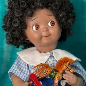 May include: A vintage doll with dark curly hair, brown eyes, and a smiling expression. The doll wears a blue and white gingham dress with a white collar and holds a wooden rocking horse toy. The text "DOLL KINGDOM US" is at the bottom.