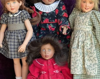 May include: Four handcrafted dolls with detailed facial features and realistic hair. The dolls are dressed in various vintage-style outfits, including plaid dresses and floral patterns. The dolls are posed against a purple background, showcasing their unique designs.