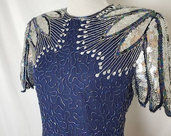 Könnte beinhalten: Ein marineblaues Paillettenkleid mit silbernen und schillernden Pailletten. Das Kleid hat einen runden Ausschnitt und kurze Ärmel. Die Pailletten sind in einem Muster aus Blättern und Wirbeln angeordnet.