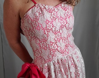 Könnte beinhalten: Ein weißes Spitzenkleid mit rosa Satin-Futter und einer rosa Satin-Schleife. Das Kleid hat einen herzförmigen Ausschnitt und ein tailliertes Oberteil. Der Rock ist weit und fließend.