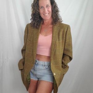 May include: A brown plaid blazer with a green lining. The blazer has a single gold button closure. The person in the image is wearing a pink crop top and light blue denim shorts.