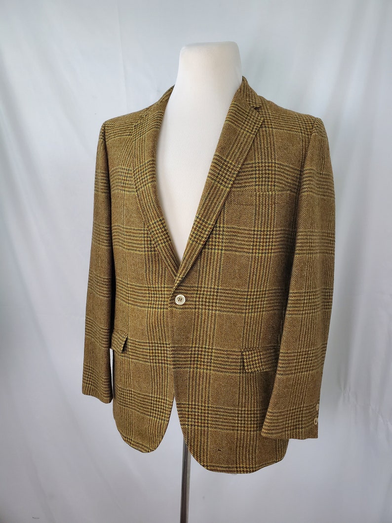 May include: A brown and yellow plaid blazer displayed on a mannequin. The blazer has a two-button closure, notched lapels, and two front pockets. The fabric has a textured appearance.