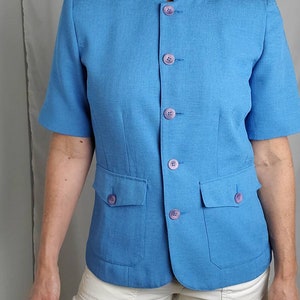 May include: A blue short-sleeved blazer with a mandarin collar and six purple buttons. The blazer has two flap pockets on the front.