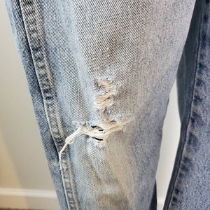 K&ouml;nnte beinhalten: Hellblaue Jeans aus Denim mit einem ausgefransten Loch am linken Bein.