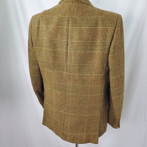 May include: A brown and tan plaid blazer displayed on a mannequin. The blazer has a classic design with a two-button closure and notched lapels. The fabric has a textured appearance, and the plaid pattern is a mix of brown, tan, and black.