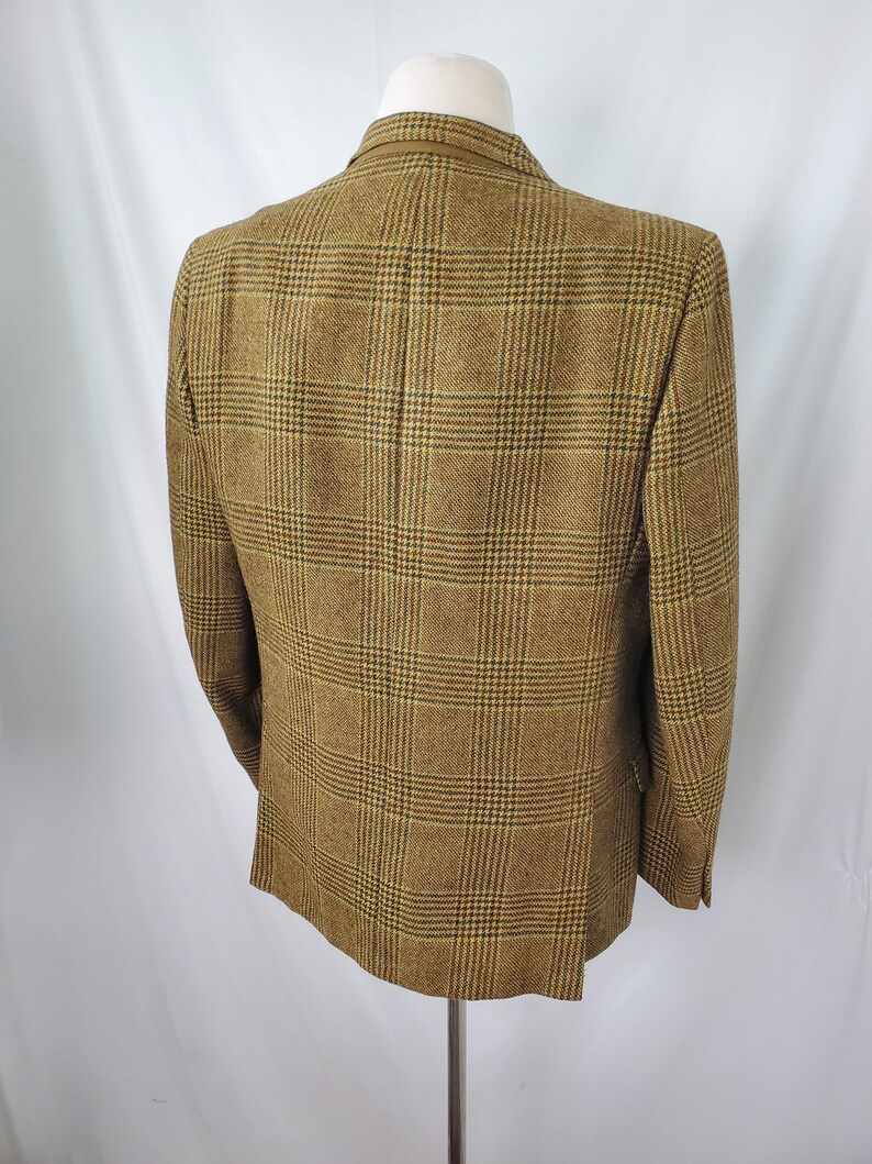 May include: A brown and tan plaid blazer displayed on a mannequin. The blazer has a classic design with a two-button closure and notched lapels. The fabric has a textured appearance, and the plaid pattern is a mix of brown, tan, and black.