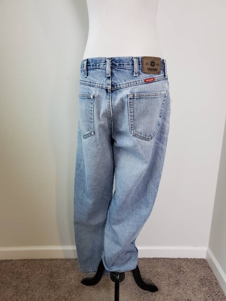 K&ouml;nnte beinhalten: Hellblaue Jeans aus Denim mit einem braunen Leder-Patch, auf dem hinten "Wrangler" steht. Die Jeans haben eine lockere Passform und ein gerades Bein.