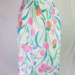 May include: A white skirt with a floral print featuring pink, blue, and green flowers. The skirt is knee-length and has a fitted silhouette.