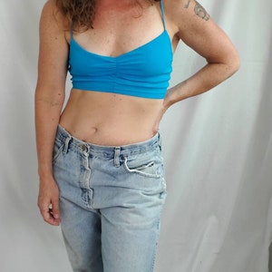 K&ouml;nnte beinhalten: Eine Frau tr&auml;gt ein hellblaues Crop-Top und eine hellblaue Jeans mit einem ausgefransten Knie.