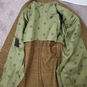 May include: A brown and tan plaid blazer with a green interior lining. The lining features a repeating pattern of small, dark green circular designs. The blazer is open, revealing the interior construction and details.