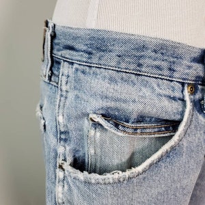 K&ouml;nnte beinhalten: Hellblaue Jeans aus Denim mit einer ausgefransten Tasche und einer hellen Waschung. Die Jeans sind abgetragen und haben einen Used-Look.