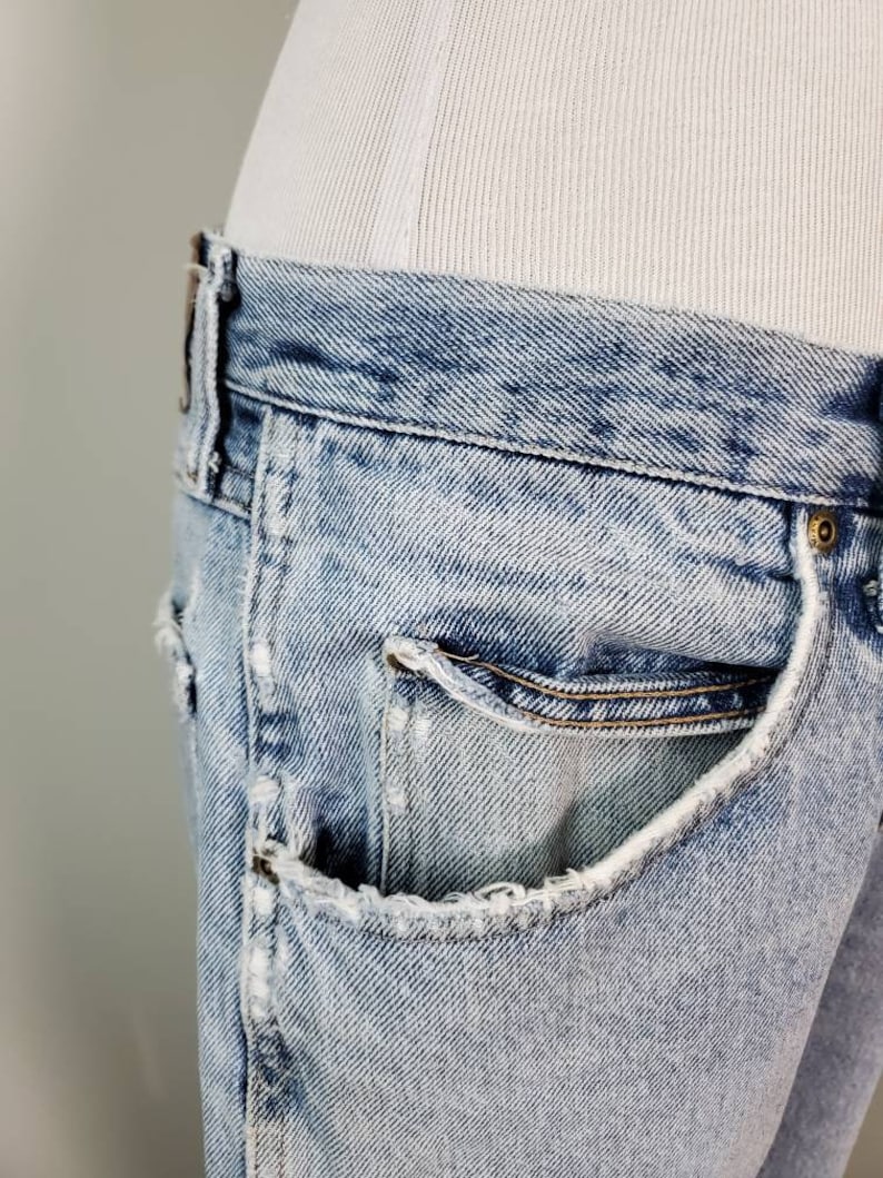 K&ouml;nnte beinhalten: Hellblaue Jeans aus Denim mit einer ausgefransten Tasche und einer hellen Waschung. Die Jeans sind abgetragen und haben einen Used-Look.