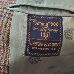May include: Close-up of the interior of a tweed jacket. The lining is olive green with a repeating pattern. A navy blue label reads "Botany" 500 BRAND Tailored by Daroff, and "LIMEHOUSE MEN'S STORE ORANGEBURG, S.C."