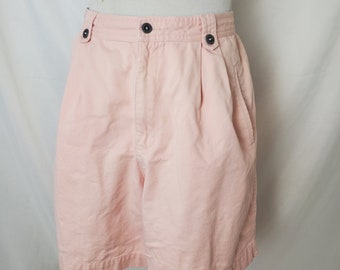 Puede incluir: Un pantalón corto de algodón rosa claro con cierre de botón y dos botones de cierre en la cintura. El pantalón corto tiene un frente plisado y dos bolsillos laterales.