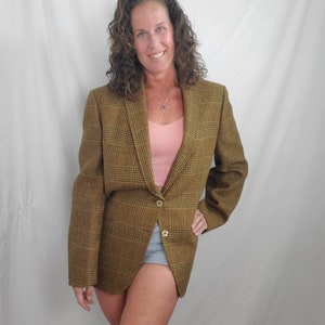 May include: A brown and black plaid blazer with two gold buttons. The blazer is worn over a pink tank top and denim shorts. The blazer has a classic, tailored design.