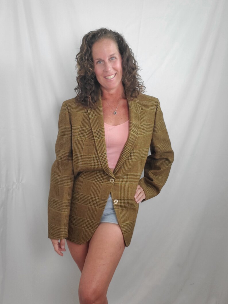 May include: A brown and black plaid blazer with two gold buttons. The blazer is worn over a pink tank top and denim shorts. The blazer has a classic, tailored design.