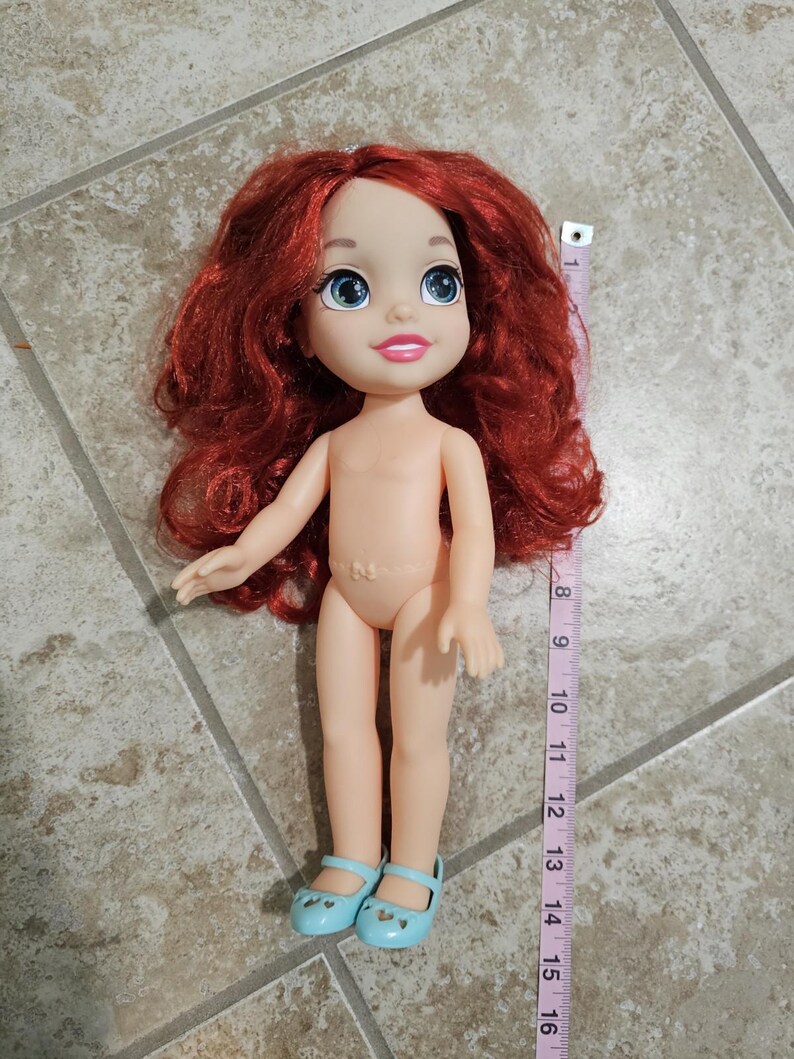 May include: A doll with red hair, blue eyes, and light blue shoes. The doll is approximately 15 inches tall. A measuring tape is next to the doll.