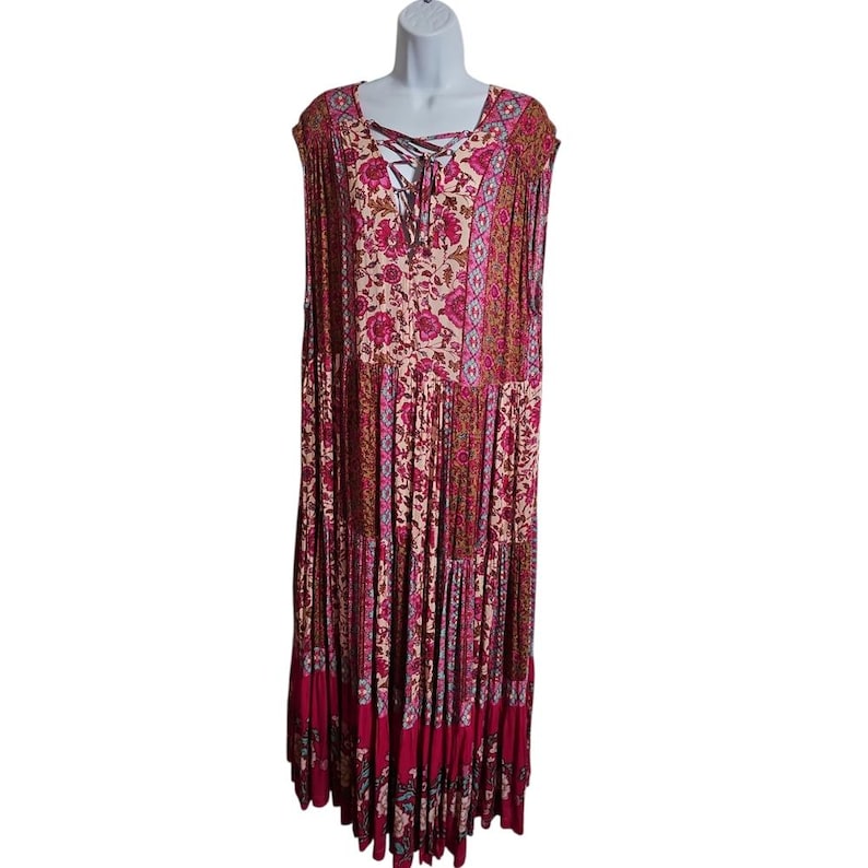 May include: A long, sleeveless dress with a floral pattern in shades of pink, red, and beige. The dress features a lace-up neckline and a tiered skirt. The dress is displayed on a white mannequin.