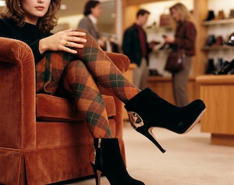 May include: Black high-heeled ankle boots with gold accents. The boots have a platform sole and a stiletto heel. The person is wearing argyle patterned tights in shades of brown, green, and orange.