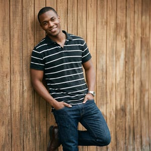 May include: A short-sleeved polo shirt featuring a black base with horizontal white stripes, a collared neckline with a button placket, paired with dark blue denim jeans, a silver chain necklace, and a silver wristwatch on the left wrist.