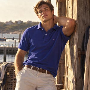 Peut inclure: Un polo bleu roi à manches courtes avec un petit logo brodé sur la poitrine, associé à un short chino beige et une ceinture en cuir marron dotée d'une boucle en métal argenté. Le polo présente un col classique et une patte à deux boutons.
