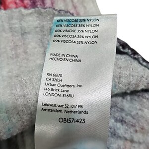 Puede incluir: Primer plano de una etiqueta de ropa con el texto "65% VISCOSE 35% NYLON" repetido varias veces. La etiqueta tambi&eacute;n incluye "MADE IN CHINA", la marca "Urban Outfitters, Inc.", y la direcci&oacute;n "146 Brick Lane LONDON, EI 6RU". El c&oacute;digo de la etiqueta es OB1571423.