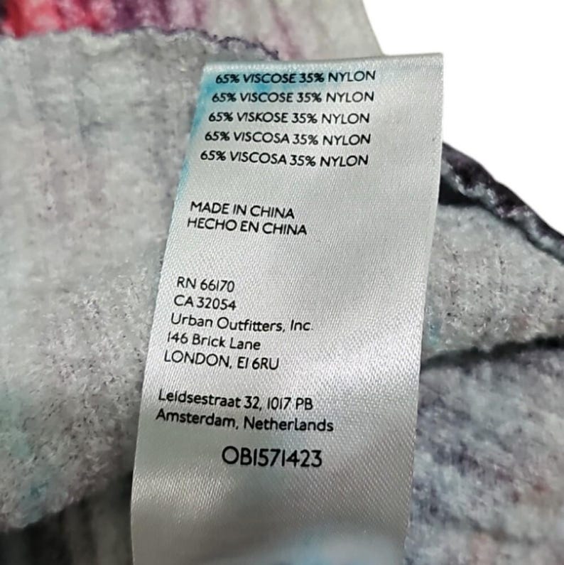 Puede incluir: Primer plano de una etiqueta de ropa con el texto "65% VISCOSE 35% NYLON" repetido varias veces. La etiqueta tambi&eacute;n incluye "MADE IN CHINA", la marca "Urban Outfitters, Inc.", y la direcci&oacute;n "146 Brick Lane LONDON, EI 6RU". El c&oacute;digo de la etiqueta es OB1571423.