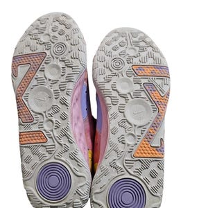 May include: A pair of athletic shoes, viewed from the soles. The soles are primarily light gray with orange and purple accents. The design includes a large "Z" shape and circular patterns. The shoe uppers are pink and purple.