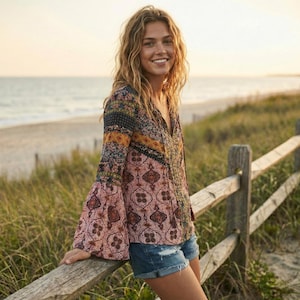 Puede incluir: Una blusa estampada con mangas acampanadas y cuello en V. La blusa presenta una mezcla de diseños florales y geométricos en tonos rosa, azul y amarillo. Llevada con shorts de mezclilla, el atuendo está en una playa.