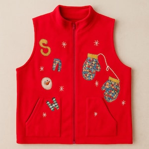 Op de afbeelding: Een rode fleece vest met een volledige ritssluiting en twee zakken. Het vest is versierd met het woord "SNOW", een sneeuwpop, sneeuwvlokken en twee wanten met een sterrenpatroon. Een feestelijk kledingstuk met winterthema.