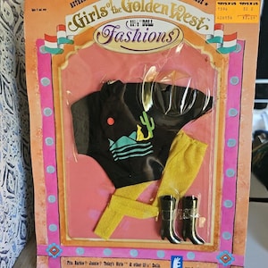 May include: A plastic package containing a doll outfit for an 11 1/2 inch doll. The outfit is a black shirt with a desert scene and a cactus, yellow trousers, and black boots. The package is pink and white with the words "Girls of the Golden West" and "11 1/2" doll fashions" printed on it.