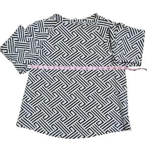 May include: A black and white geometric patterned top with short sleeves. The top is measured with a pink measuring tape, showing a length of approximately 18 inches.