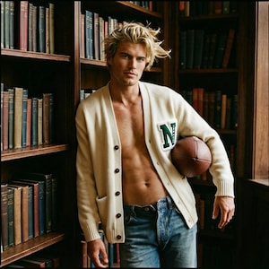 May include: Cream-colored cardigan sweater with a green "N" patch, paired with blue jeans. The sweater has button closures and pockets. A brown football is held in the arm. The background features a bookshelf filled with books.
