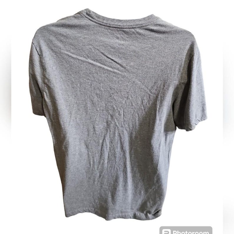 Pu&ograve; includere: Una maglietta grigio melange a maniche corte. La maglietta ha uno scollo tondo ed &egrave; realizzata in un tessuto morbido e strutturato. Il retro della maglietta &egrave; visibile, mostrando lo scollo e le spalle.