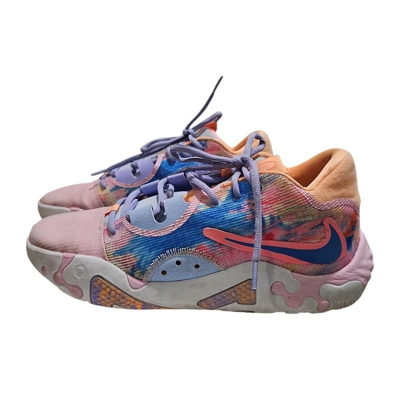 May include: A pair of colorful sneakers with a tie-dye pattern. The shoes feature a pink, blue, and orange color scheme with a blue Nike swoosh. The laces are purple and orange. The soles are white and pink.