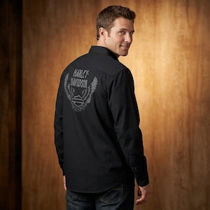 Może przedstawiać: Czarna koszula z długim rękawem z logo Harley-Davidson nadrukowanym na plecach. Logo zawiera nazwę marki, skrzydła i emblemat tarczy. Koszula jest wykonana z ciemnej tkaniny i ma zapięcie na guziki.