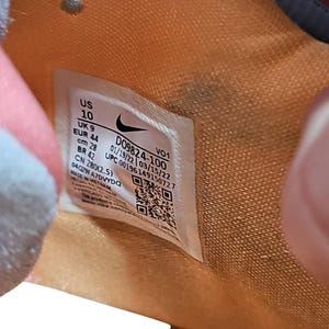 May include: Close-up of a shoe's interior with a white label. The label displays the size as US 10, UK 9, EUR 44, and a measurement of 28 cm. The label also includes the style code D09824-100 and a UPC code.