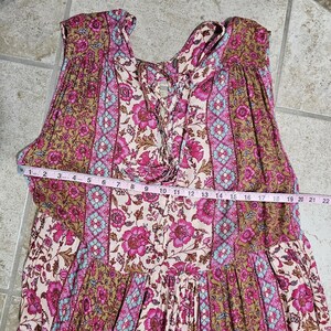May include: A sleeveless dress with a floral pattern in shades of pink, brown, and blue. The dress features a lace-up neckline and a tiered skirt. A measuring tape is laid across the dress, showing a measurement of 22 inches.