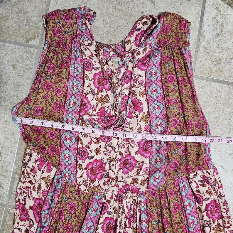 May include: A sleeveless dress with a floral pattern in shades of pink, brown, and blue. The dress features a lace-up neckline and a tiered skirt. A measuring tape is laid across the dress, showing a measurement of 22 inches.