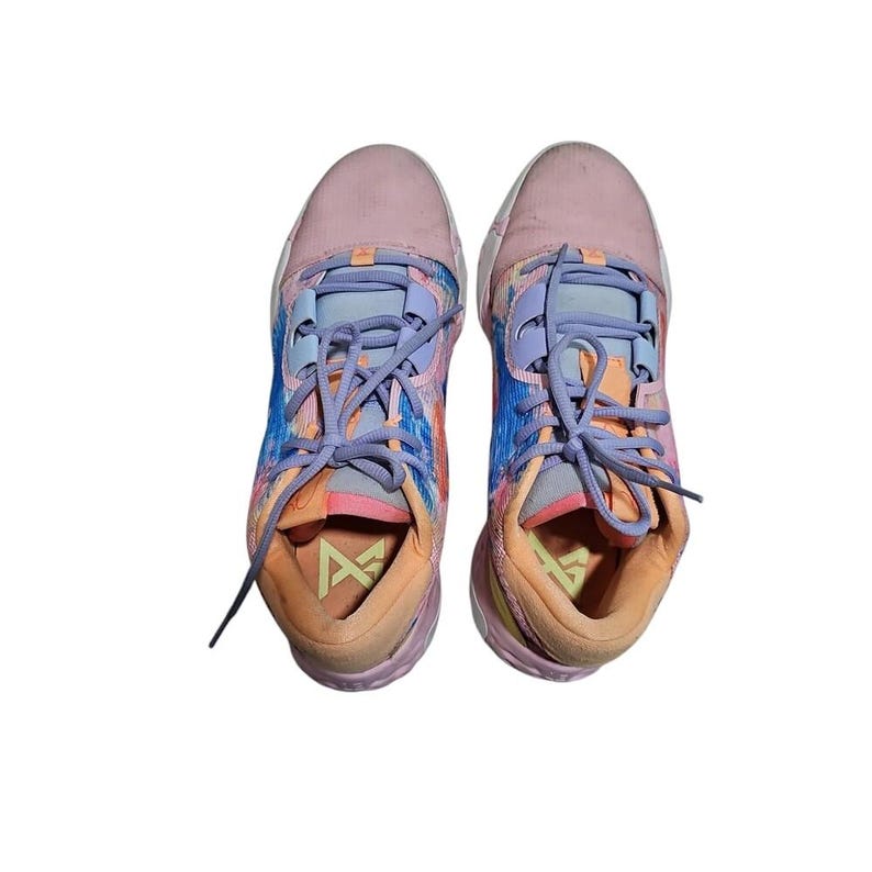 May include: A pair of colorful athletic shoes with a mix of pink, blue, and orange hues. The sneakers feature a lace-up design with light purple laces and a logo on the tongue. The soles are a light orange color.