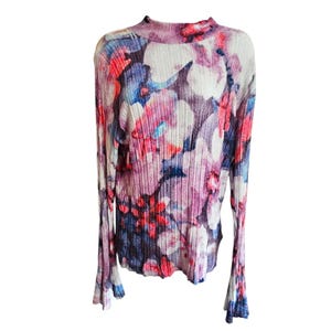 Puede incluir: Una blusa de manga larga con cuello alto. La blusa presenta un estampado floral en tonos rosa, morado, azul y blanco. La tela tiene una textura acanalada. Las mangas se ensanchan en las mu&ntilde;ecas.