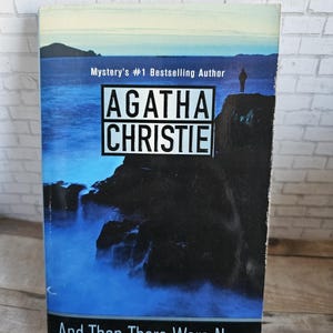 以下が含まれることがあります： アガサ・クリスティ著「そして誰もいなくなった」というタイトルのペーパーバック。表紙には、崖の上に人物がいる青と黒の風景が描かれています。「Mystery's #1 Bestselling Author」というテキストも表示されています。