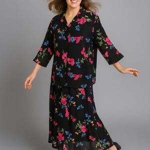 May include: A black floral print two-piece outfit. The set includes a button-down shirt with three-quarter sleeves and a matching skirt. The floral pattern features pink, blue, and green accents. The outfit is paired with black heels.