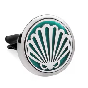May include: A silver car air vent diffuser with a teal and white seashell design. The diffuser has a black clip for attachment and a circular shape. The seashell design is in the center of the diffuser.