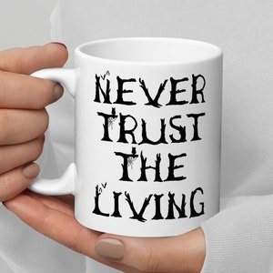 May include: White ceramic mug with a black graphic that reads "Never Trust The Living".