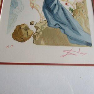 Pu&ograve; includere: Una stampa incorniciata di un dipinto con una figura blu e bianca in primo piano. La figura &egrave; in piedi su una superficie rocciosa. Lo sfondo &egrave; un cielo azzurro e bianco chiaro. La stampa &egrave; firmata "E.A." e "Dali" nell'angolo in basso a destra.