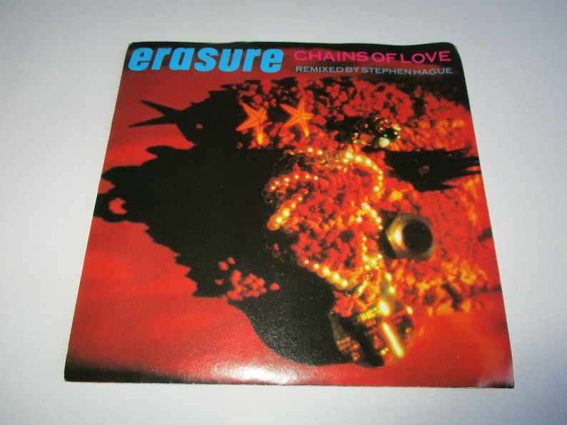 May include: A red and orange vinyl record with the text "Erasure" and "Chains of Love" in blue and white. The text "Remixed by Stephen Hague" is in smaller white text. The record cover features a close-up of a red and orange object with a pearl necklace and a starfish.