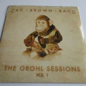 May include: A vintage vinyl record album cover featuring a brown monkey wearing a red and white shirt and holding a hat. The album is titled "The Grohl Sessions Vol. 1" by Zac Brown Band.